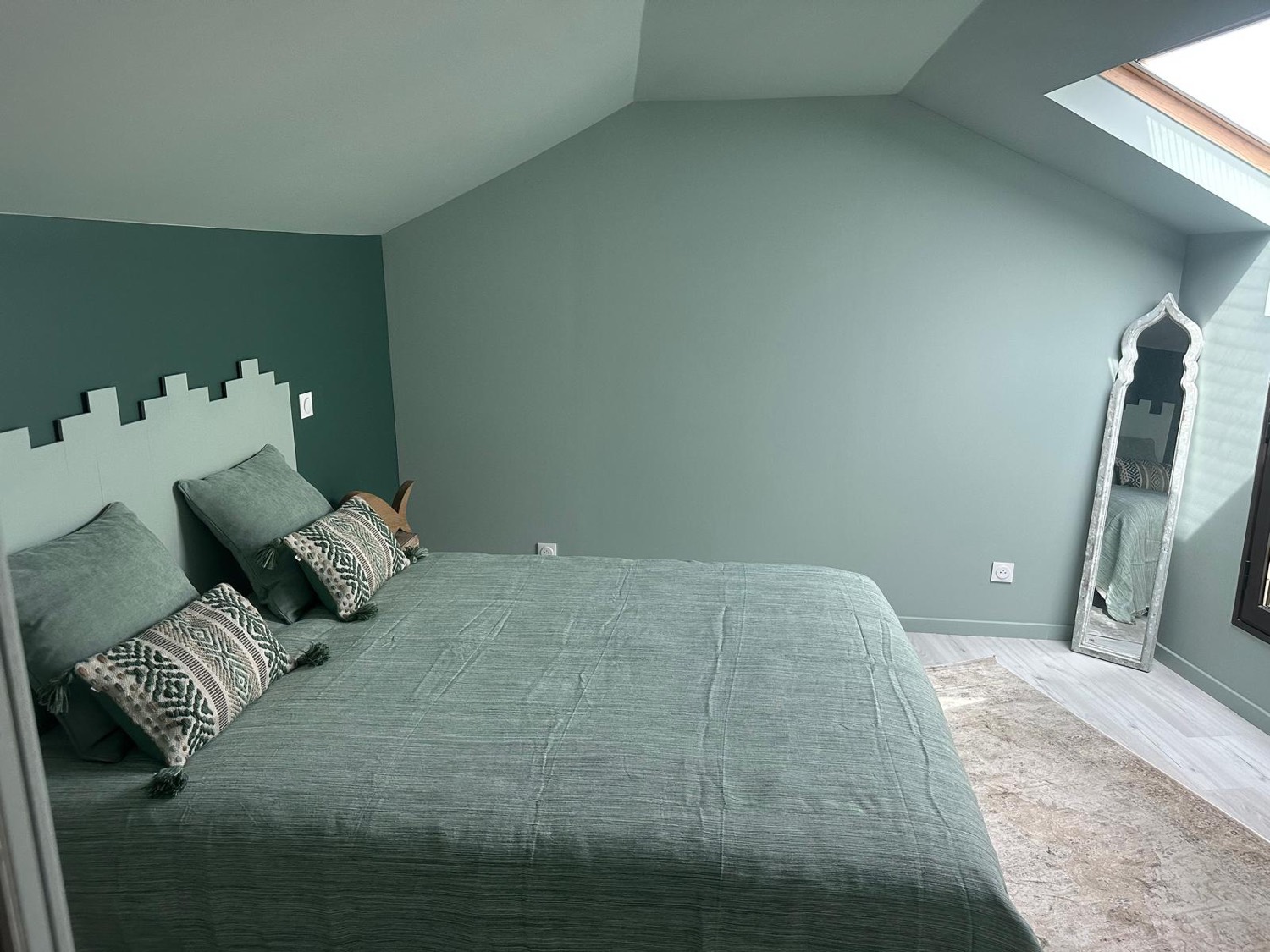 Chambre bord de mer aux murs vert sauge bicolores, grand miroir sur pied et sol stratifié clair