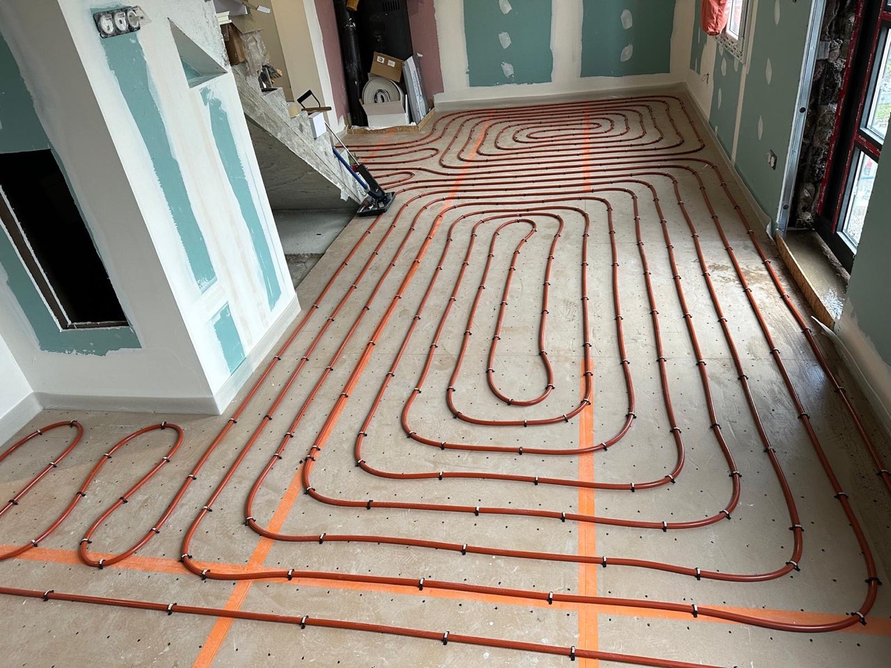 Pose d'un plancher chauffant hydraulique : boucles de tubes fixées sur la dalle d'une pièce en cours de rénovation — chantier à Beuzeville