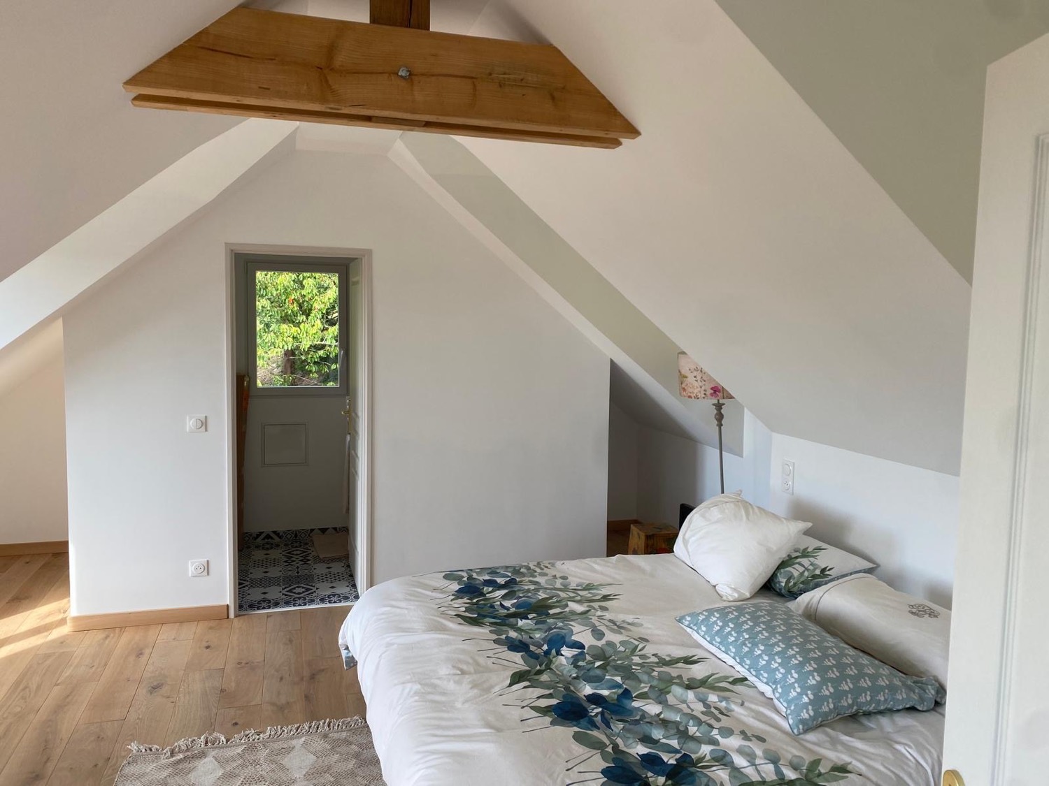 Chambre sous combles avec charpente bois apparente, parquet chêne et accès à la salle d'eau