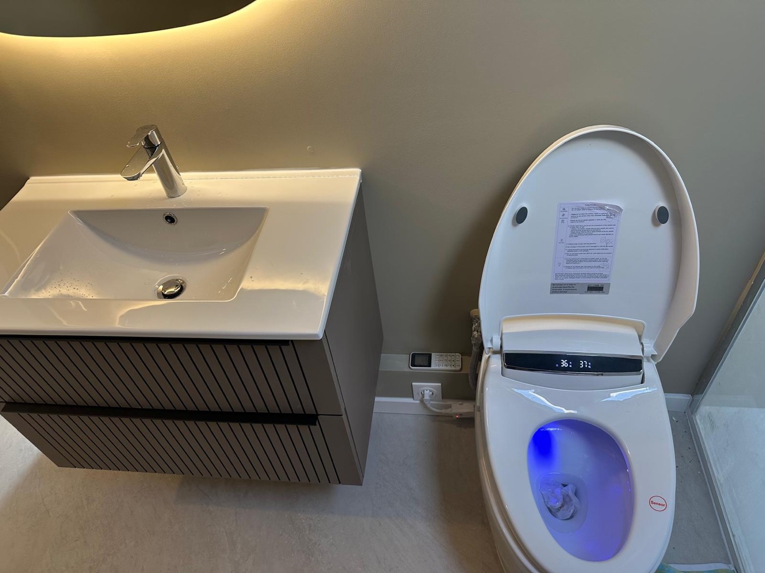 WC japonais lavant avec abattant chauffant, écran de température et commandes déportées, près du meuble vasque nervuré