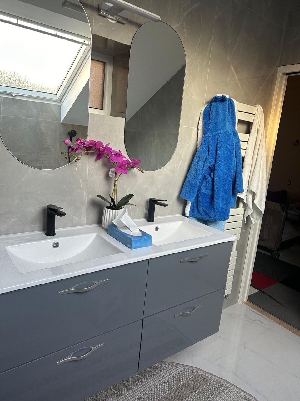 Meuble double vasque gris avec miroirs ovales et robinetterie noire dans la salle de bain de Lisieux